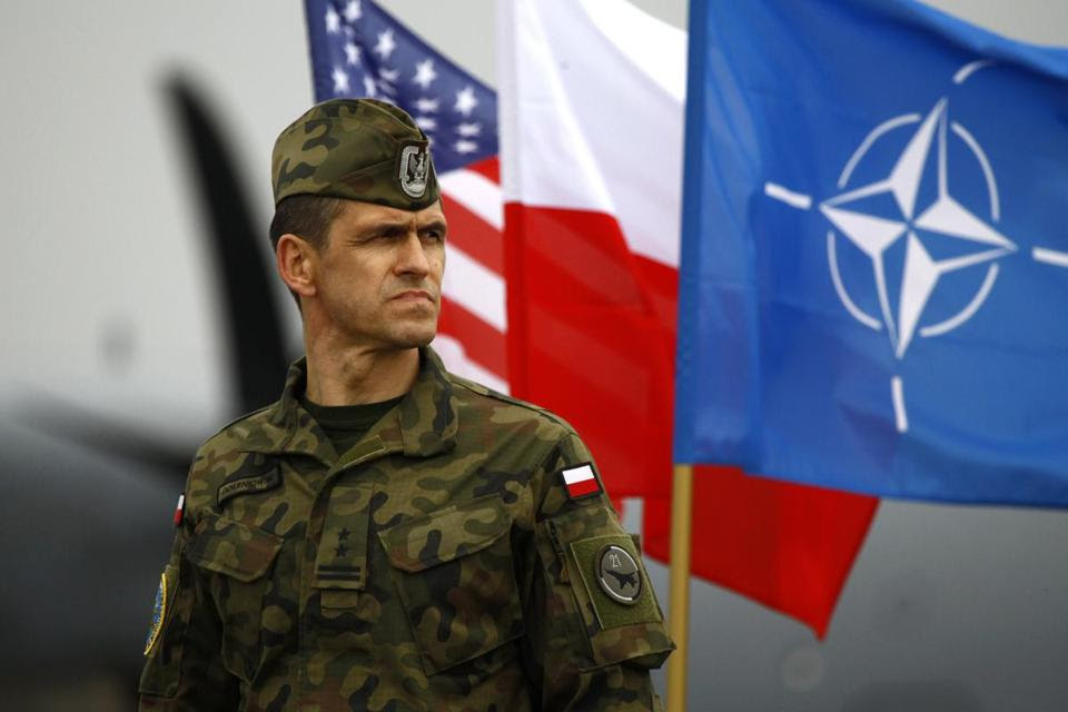 A Polish soldier stands near US, Poland, and NATO flags as US paratroopers arrive to participate in training exercises in April.